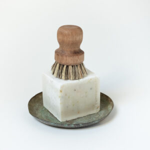 cube de savon ménager posé sur une coupelle en cuivre et surmonté d'une brosse à vaisselle