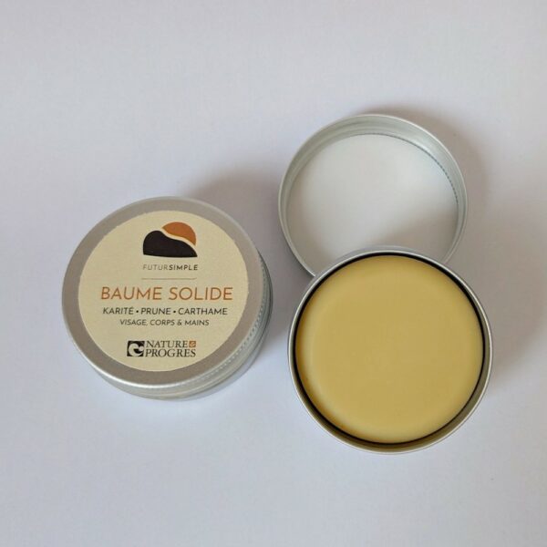 baume solide de couleur jaune clair. à côté se trouve sa boîte en aluminium avec étiquette dans les tons crème, orangé et marron ; logo futur simple