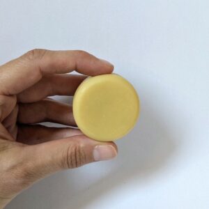 baume solide, de couleur jaune clair, tenu dans une main entre le pouce et l'index