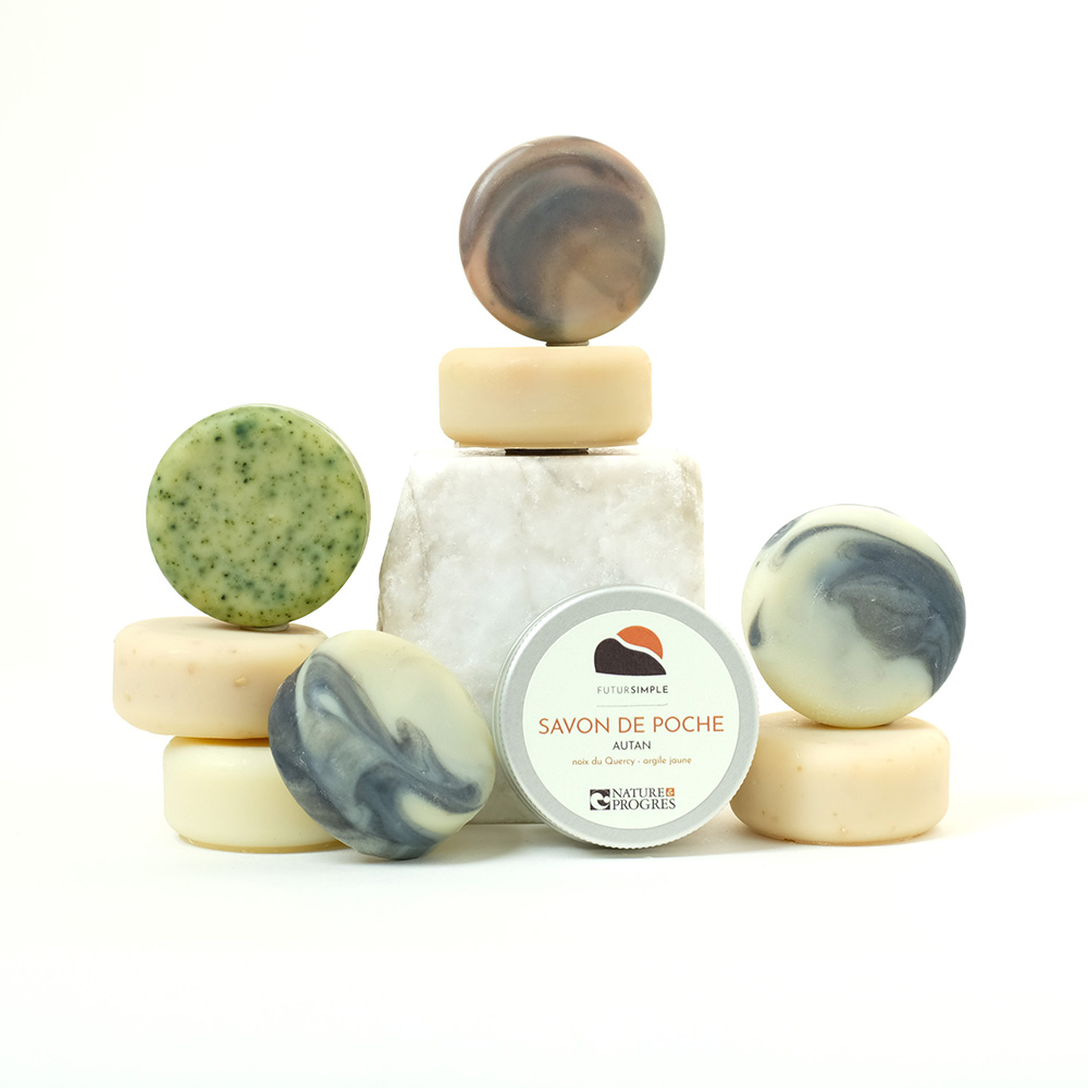 savon de rasage ouvert, posé sur un bloc de marbre blanc. dessous, le couvercle de la boîte aluminium, étiquette bleu ciel. photo sur fond blanc